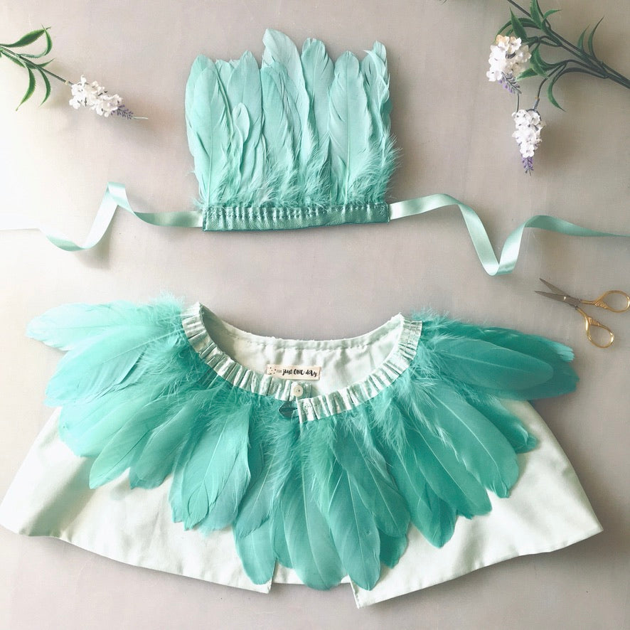 flat lay of child's mint green feather cape and feather headdress