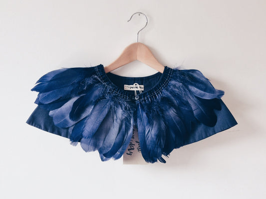 child's indigo blue feather cape on a wooden hanger against a white wall