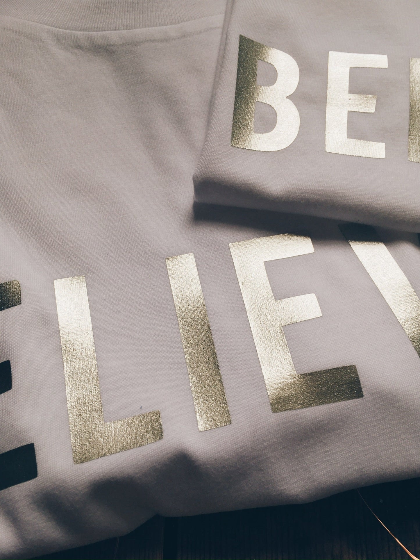 Close up of metallic gold print on white Believe t-shirt by For Just ONE Day