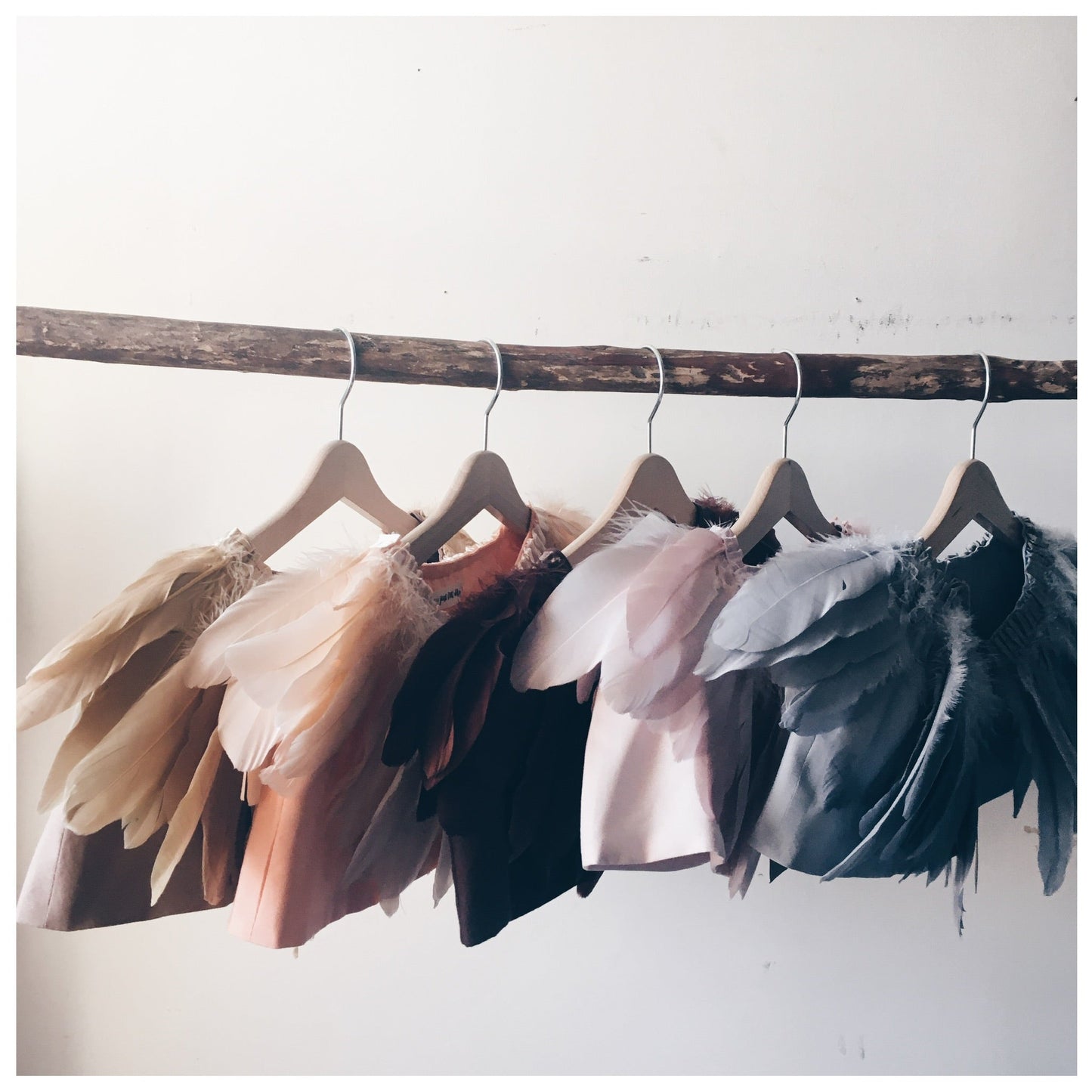 feather capes in boho rainbow colours hanging on a stick 