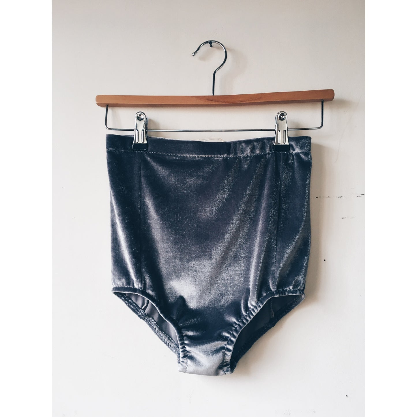 grey velvet high waisted 'booty' shorts on a wooden hanger against a white wall