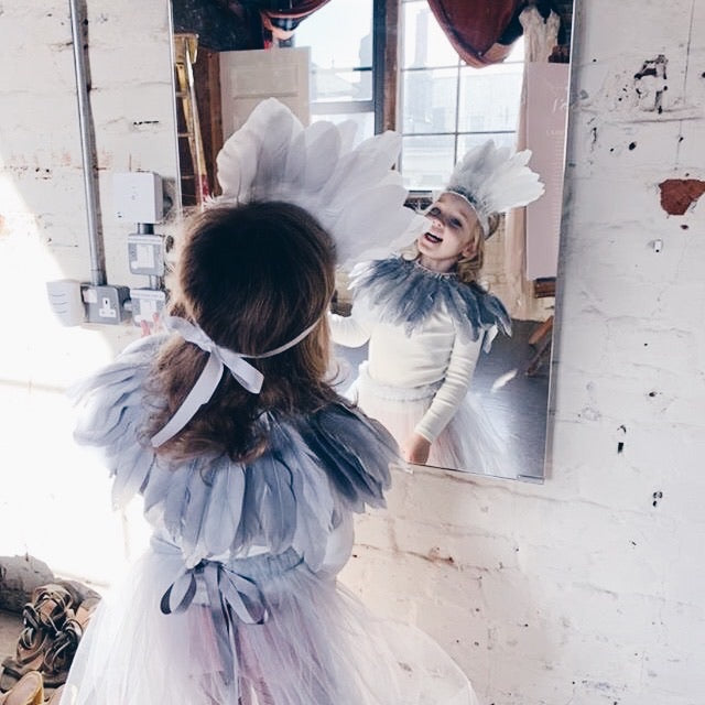 Girl looking at her refection in the mirror, wearing a grey feather headdress, grey feather cape, Titania tulle tutu by For Just ONE Day 