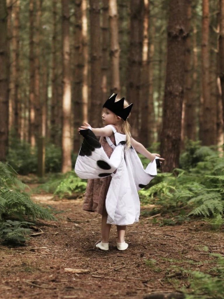 Child in a forest wearing white butterfly wings and a black crown