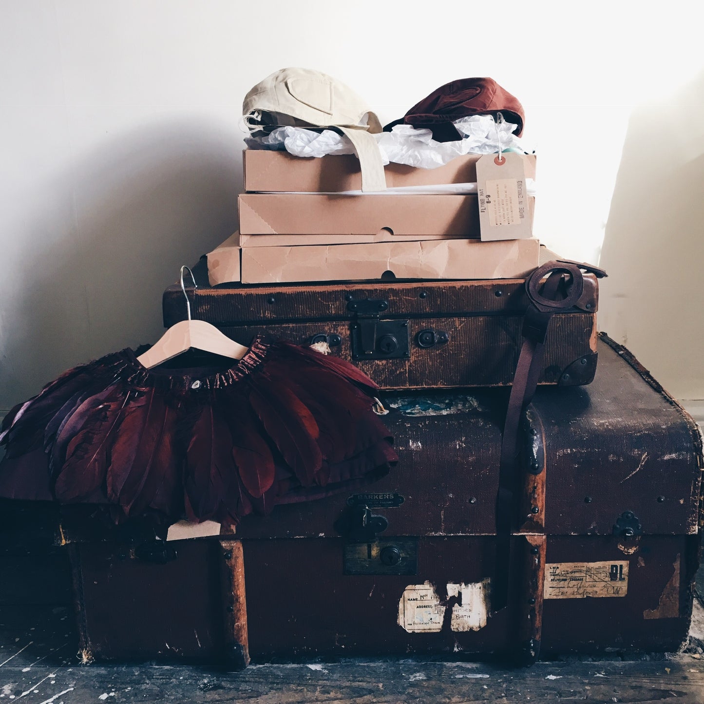 A brown feather cape, brown leather flying goggles & two flying hats styled on Vintage luggage.