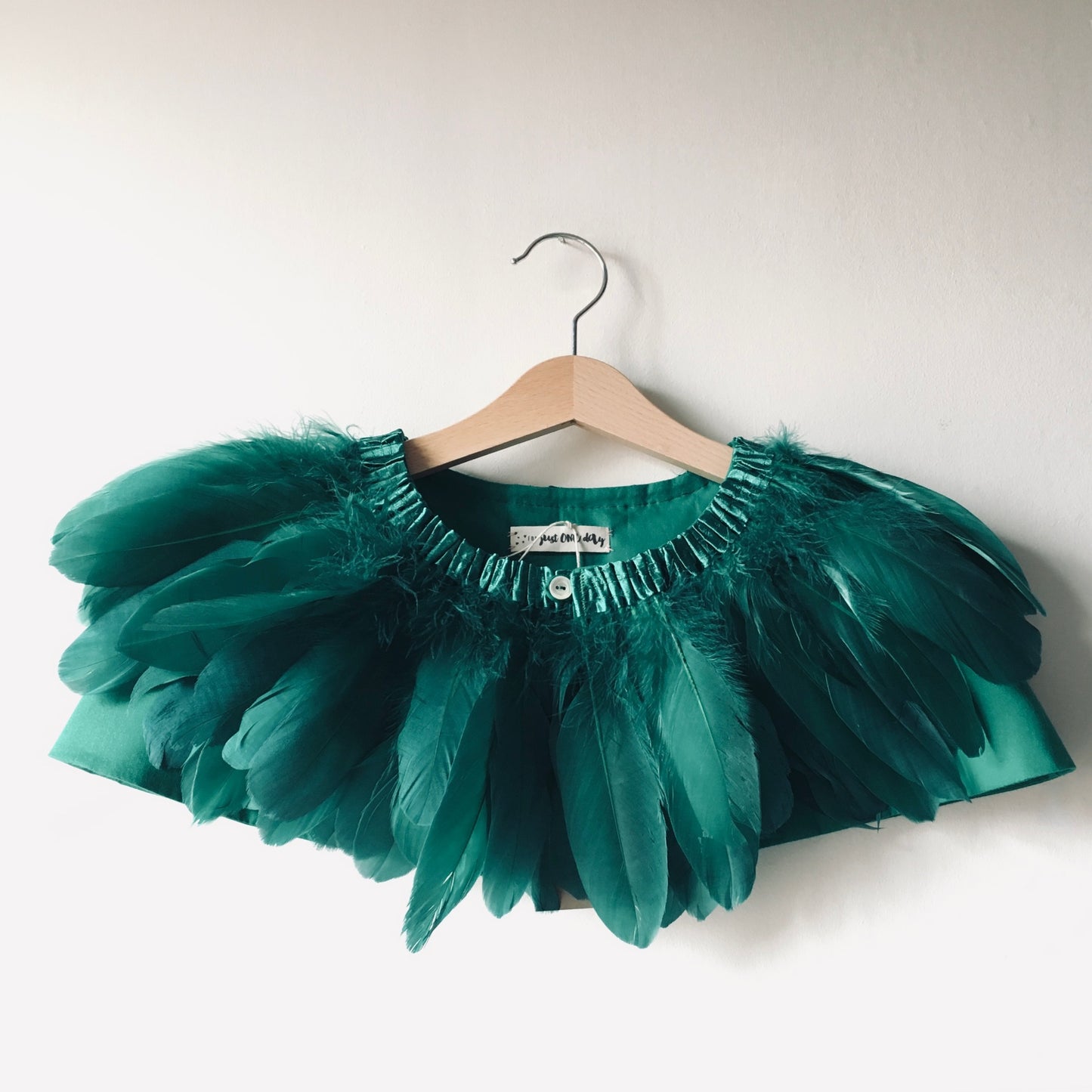 Emerald green feather cape on wooden hanger