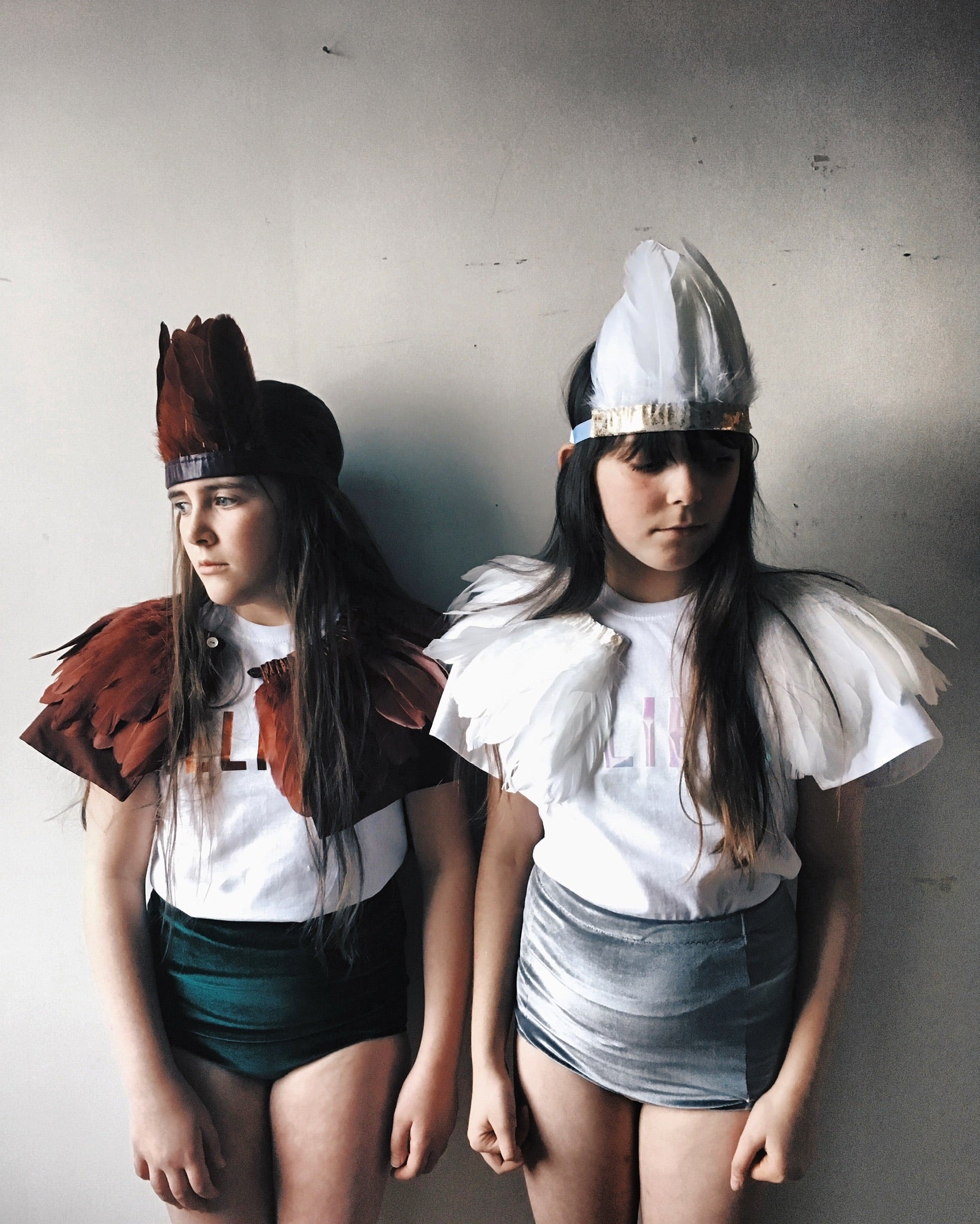 Two girls wearing woodland warrior costumes by For Just ONE Day. feather headdress, feather cape, believe t-shirt, Velvet shorts