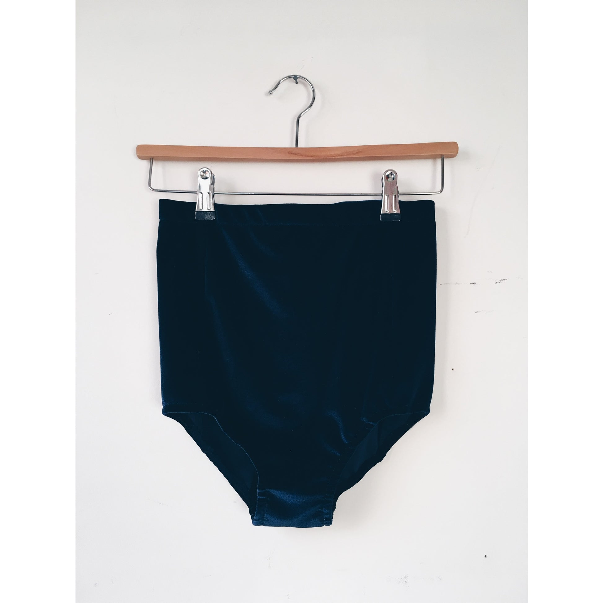 Midnight blue hight waisted velvet shorts on a wooden hanger against a white background