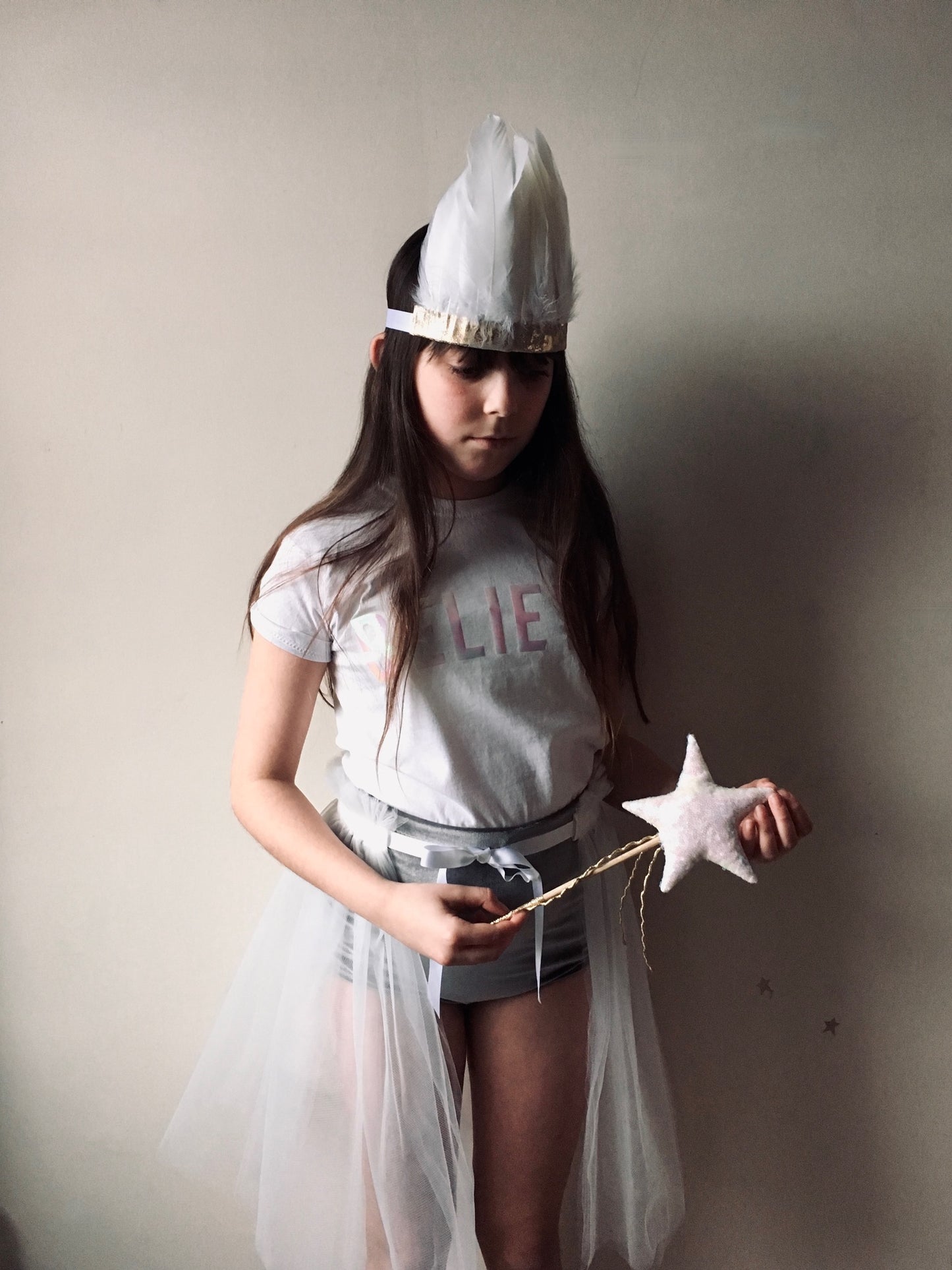 Girl holding a sequin star wand, wearing a white feather and metallic gold leather headdress, believe t-shirt, velvet shorts and tulle tutu, by For Just ONE Day
