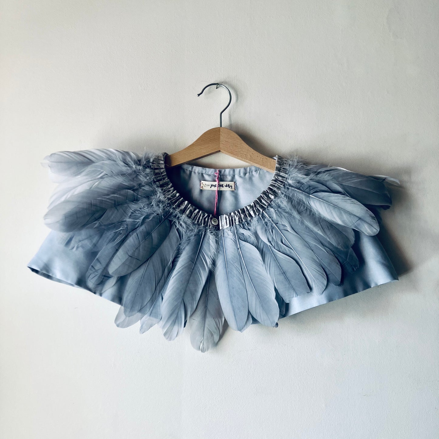 grey feather cape on wooden hanger against a white wall
