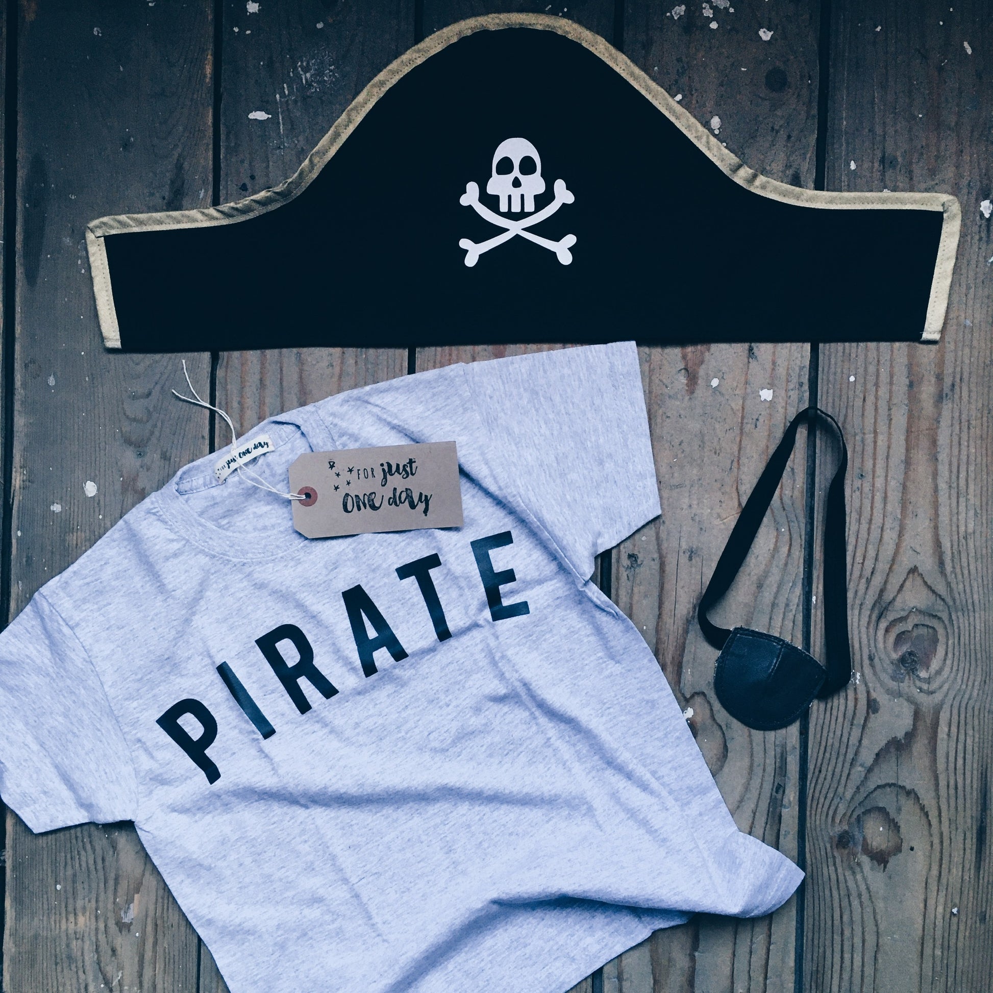 Flat-lay of child's pirate costume by For Just ONE Day - Leather Pirate eye patch, Pirate hat and grey Pirate T-shirt
