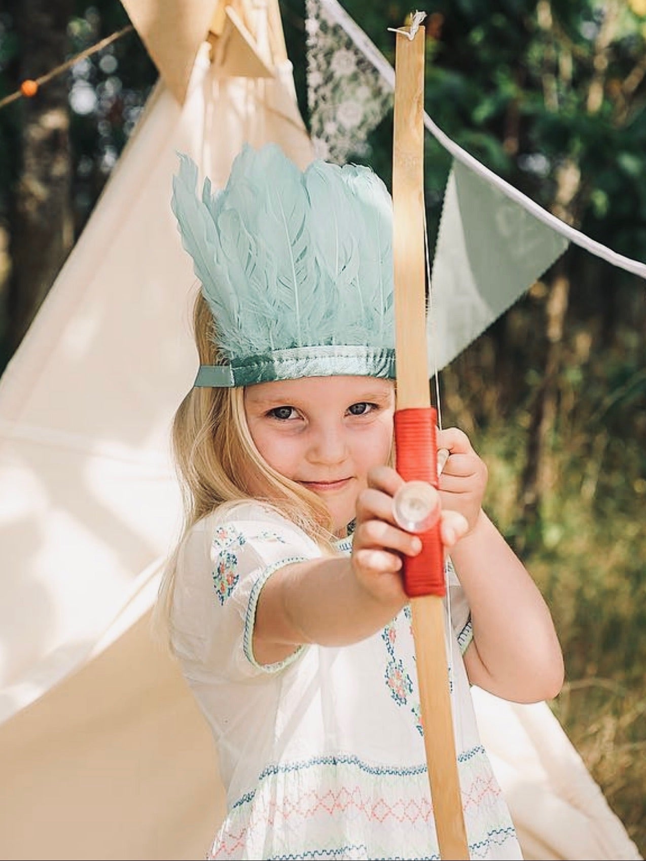 Girl shooting a bow and arrow, wearing a mint green feather and metallic leather headdress by For Just ONE Day