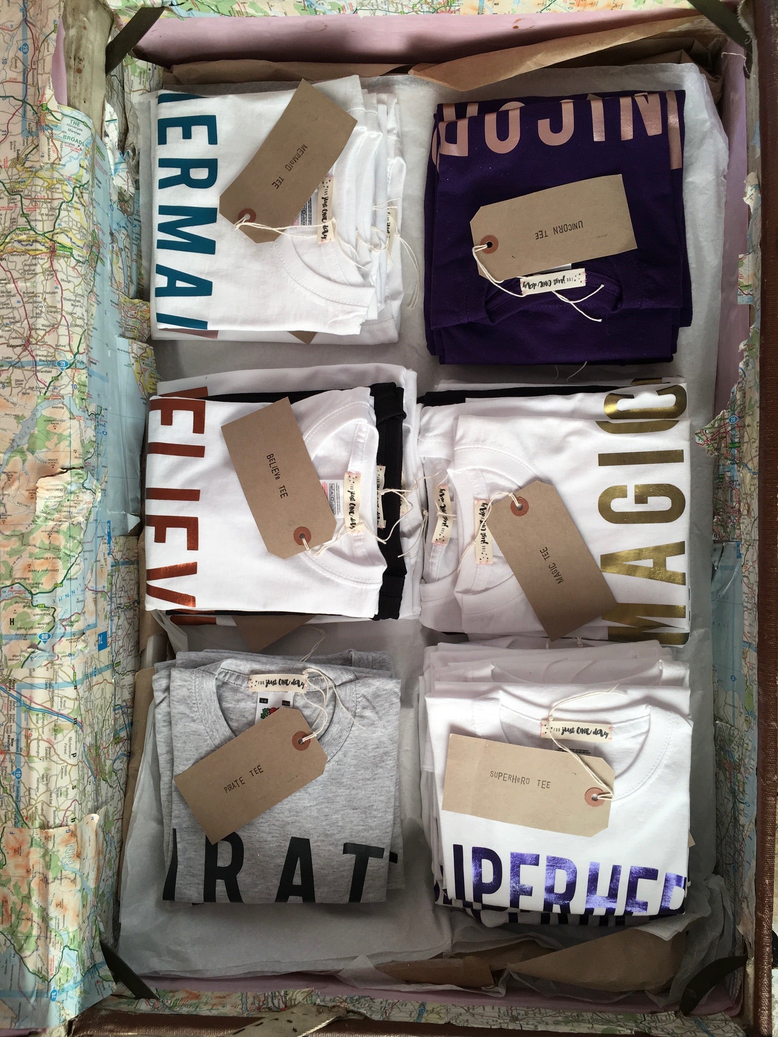 For Just ONE Day t-shirt range folded in piles inside of a travel trunk