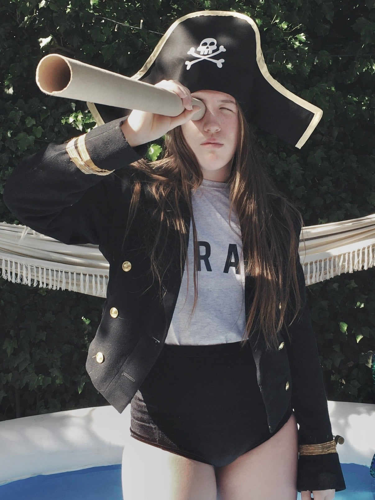 A girls wearing a pirate costume, holding a cardboard telescope to her eye
